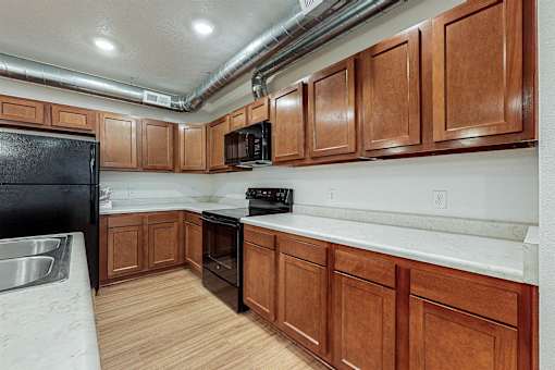 A kitchen with wooden cabinets and a black fridge at Melbourne Apartments, Des Moines