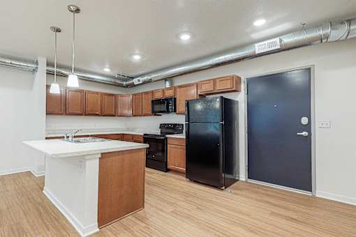 A kitchen with a black refrigerator and wooden cabinets at Melbourne Apartments, Des Moines, IA