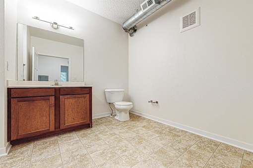 A bathroom with a toilet and a vanity with a mirror at Melbourne Apartments, Des Moines, Iowa