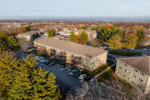 An aerial view of a parking lot and buildings with trees in the foreground. at Rosemont Place Apartments, Des Moines