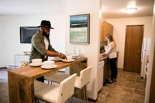 a man setting a table in a kitchen with a woman in the sink at Rosemont Place Apartments, Des Moines, IA
