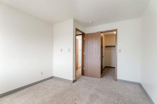 A room with a carpeted floor and a wooden door at Rosemont Place Apartments, Iowa, 50320
