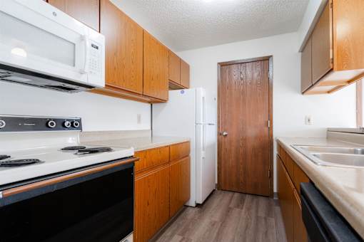 A kitchen with a black stove top oven, a white microwave, a white refrigerator, and wooden cabinets at Rosemont Place Apartments, Des Moines, IA