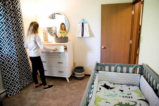 a woman standing in a nursery with a crib and a dresser at Rosemont Place Apartments, Des Moines, IA, 50320