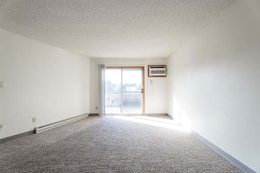 A room with a carpeted floor and a sliding glass door. at Rosemont Place Apartments, Iowa, 50320