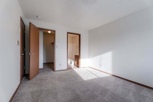 A room with a carpeted floor and white walls with a brown door. at Rosemont Place Apartments, Des Moines, 50320