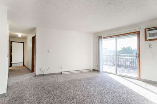 A room with a carpeted floor and a sliding glass door leading to a balcony at Rosemont Place Apartments, Iowa