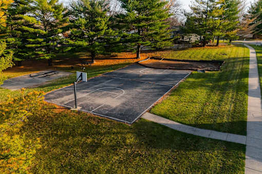 A basketball court surrounded by trees and grass. at Rosemont Place Apartments, Des Moines