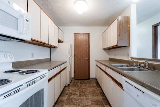 A kitchen with white appliances and brown cabinets at Rosemont Place Apartments, Iowa, 50320