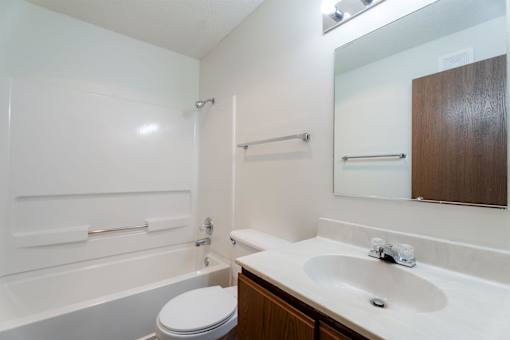 A white bathroom with a toilet, sink, and bathtub. at Rosemont Place Apartments, Iowa