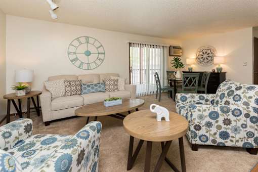A living room with a clock on the wall and a couch with a pillow on it at Rosemont Place Apartments, Des Moines