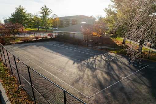 A parking lot with a fence and trees in the background. at Rosemont Place Apartments, Iowa