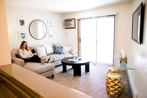 a woman sitting on a couch reading a book in a living room at Rosemont Place Apartments, Iowa, 50320