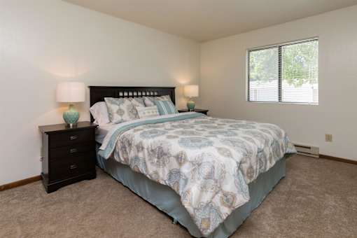 A bedroom with a bed, nightstand, and two lamps at Sutton Hill Apartments, Des Moines, 50320