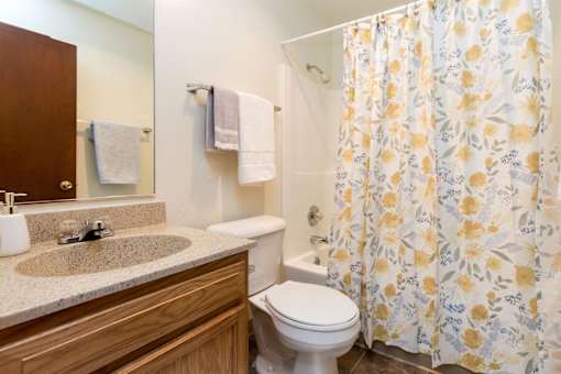 A bathroom with a toilet, sink, and shower curtain at Sutton Hill Apartments, Des Moines