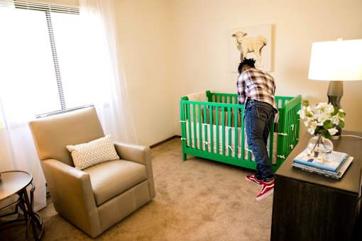 a baby in a room with a crib and a rocking chair at Sutton Hill Apartments, Des Moines, IA, 50320