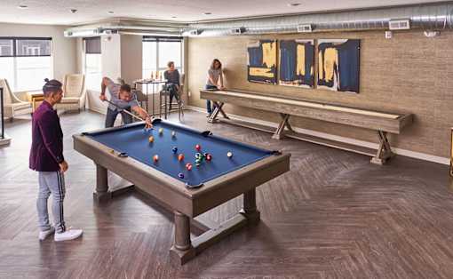 A group of people playing pool in a room with a pool table at Velocity Apartments, Des Moines, Iowa