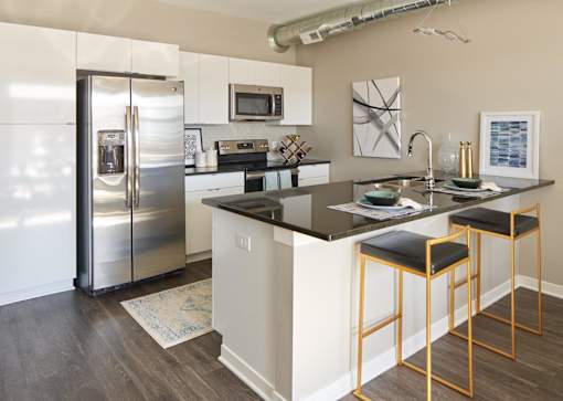 A kitchen with a refrigerator, microwave, and bar stools at Velocity Apartments, Des Moines, IA, 50309