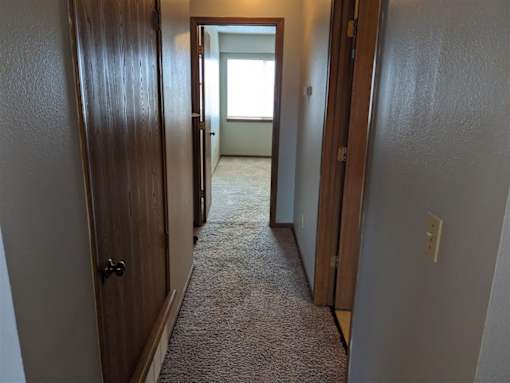 a hallway with wooden doors and a carpeted floor at Hunters Run Apartments, Newton, Iowa