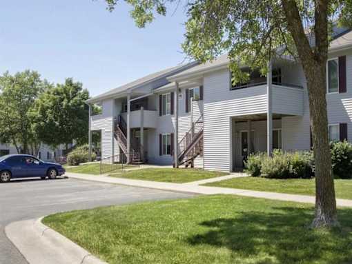 a white apartment building with a blue car parked in front at Hunters Run Apartments, Newton, IA,  50208