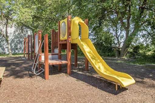 a playground with a slide and chairs in a park at Hunters Run Apartments, Newton, IA