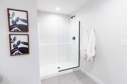 A white bathroom with a glass shower door and two framed pictures on the wall.at Plant 1 Lofts, N. Newton Iowa   
