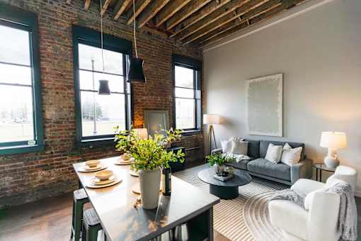 A dining room with a table set for two and a couch with a grey throw.at Plant 1 Lofts, Iowa, 50208