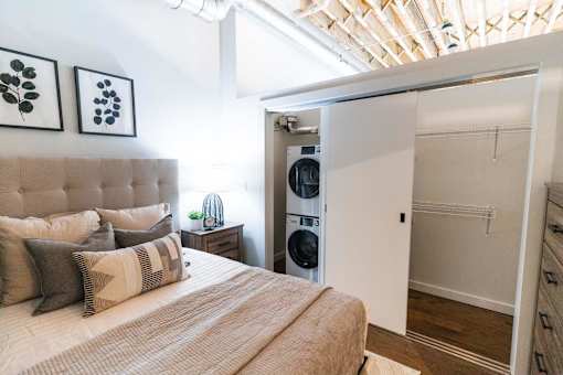 A bedroom with a bed, pillows, and a washing machine in the closet.at Plant 1 Lofts, N. Newton, IA 50208  