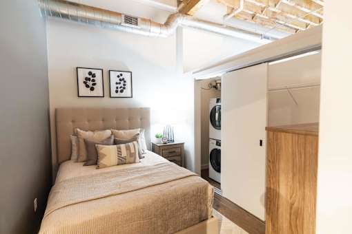 A bedroom with a bed, pillows, and a wooden cabinet.at Plant 1 Lofts, Iowa   