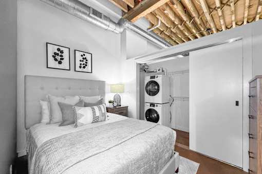 A bedroom with a bed, pillows, and a white wall with two framed pictures.at Plant 1 Lofts, N. Newton  