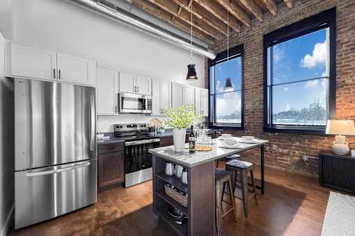 A kitchen with a stainless steel refrigerator and a brick wall.at Plant 1 Lofts, Iowa, 50208