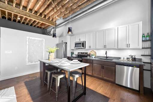 A kitchen with a table and chairs in front of a dishwasher and a microwave.at Plant 1 Lofts, N. Newton  