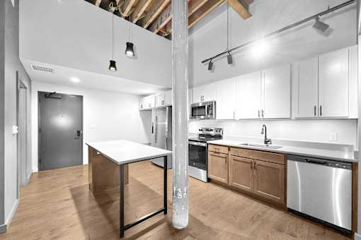 A kitchen with a white table and wooden cabinets.at Plant 1 Lofts, N. Newton, IA  