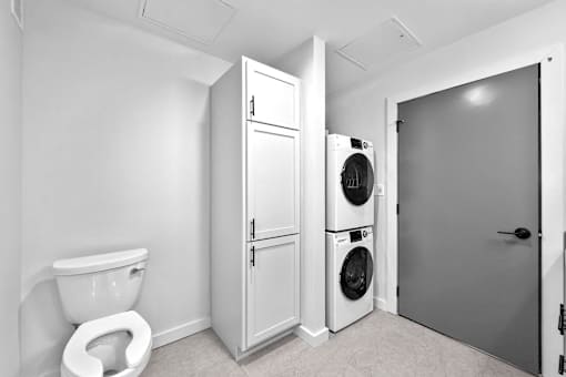 A white toilet sits next to a white cabinet and a washing machine in a laundry room.at Plant 1 Lofts, N. Newton, IA 50208  
