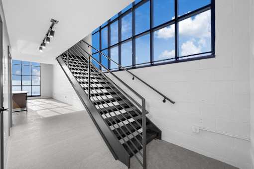 A staircase with a metal railing leads up to a window with a view of the sky.at Plant 1 Lofts, N. Newton, IA 50208  
