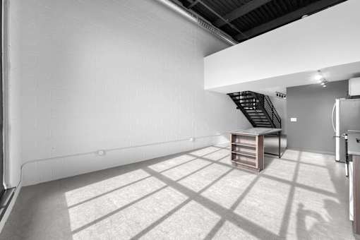 A room with a white wall and a wooden staircase.at Plant 1 Lofts, N. Newton, IA 50208  