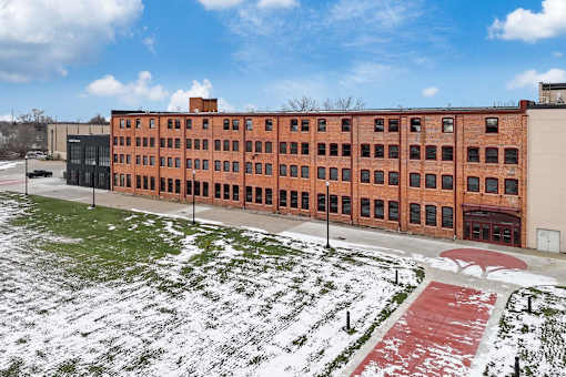 A large red brick building with a green lawn in front.at Plant 1 Lofts, N. Newton, IA 50208  