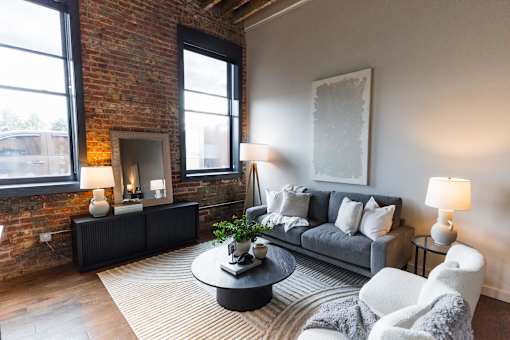 A living room with a grey couch, a black coffee table, and a fireplace with a brick wall.at Plant 1 Lofts, N. Newton Iowa   