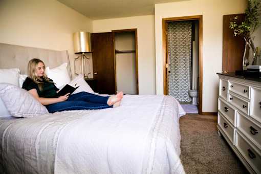 a woman sitting on a bed reading a book  at Bristol Ridge, Urbandale, IA, 50322