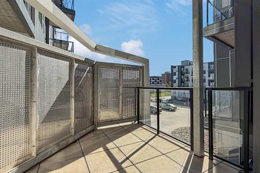 A balcony with a metal railing and glass doors overlooks a parking lot and buildings.
