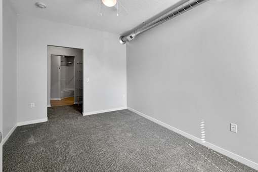 A room with a grey carpet and a white wall with a doorway leading to another room.