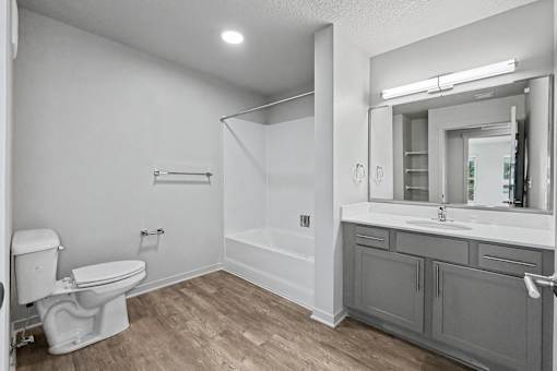 A white toilet sits in a bathroom with a wooden floor and white walls.