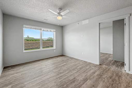 A room with a ceiling fan and a view of a field through the window.