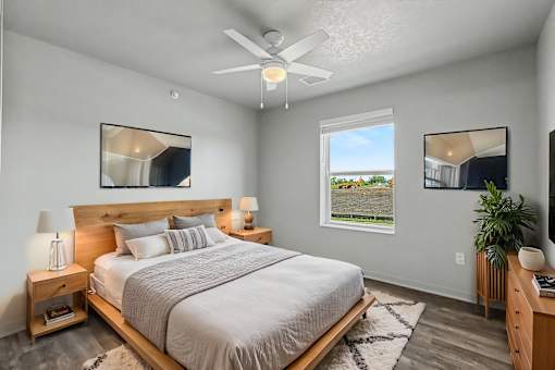 A bedroom with a large bed, a ceiling fan, and a window with a view of the outdoors.