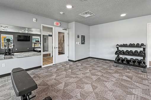 A gym room with a bench, weights, and a mirror.