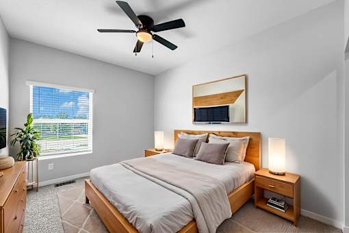 A bedroom with a large bed, a ceiling fan, and a window with a view of the sky.