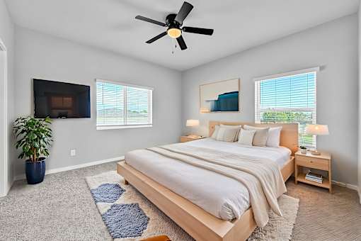 A bedroom with a large bed, a ceiling fan, and a potted plant.