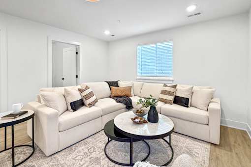 A finished basement with a living room area with a white sectional and a glass coffee table.