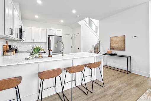 A kitchen with white cabinets and a white countertop with a bar stool in front of it.