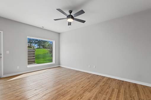 A room with a ceiling fan and a window showing a staircase and a green lawn outside.